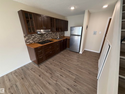 Kitchen featuring wood-finish flooring, dark wood cabinetry with glass-front uppers, a mosaic tile backsplash, and recessed lighting - #209 11429 124 St Nw, Edmonton, AB 