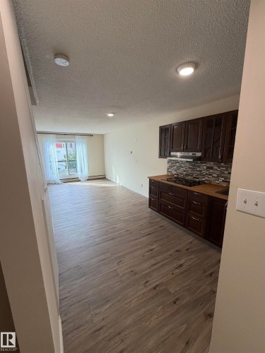 Wood-finish flooring throughout, dark wood cabinetry, mosaic tile backsplash, built-in cooktop, and recessed lighting - #209 11429 124 St Nw, Edmonton, AB 