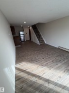 Wood-finish flooring throughout, stainless steel refrigerator, dark wood-finish cabinetry, recessed ceiling lighting, and a staircase with an ornamental metal railing - 