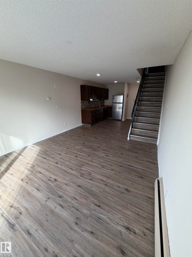 Open-concept living area featuring wood-finish flooring, dark wood cabinetry, a tiled backsplash, and stainless steel appliances - #209 11429 124 St Nw, Edmonton, AB 