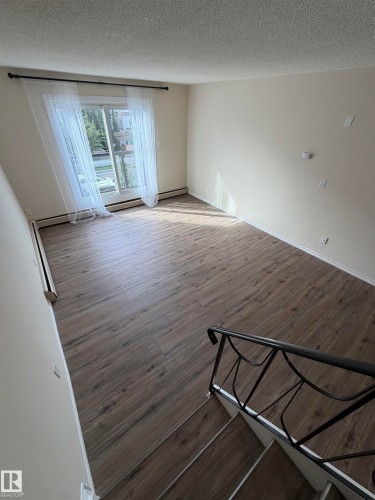 Spacious room featuring wood-finish flooring, a sliding glass door, and neutral wall paint - #209 11429 124 St Nw, Edmonton, AB 