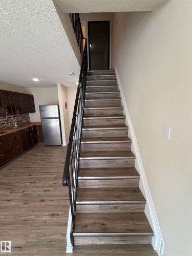 Wood-finish flooring throughout, dark wood cabinetry, stainless steel refrigerator, and a mosaic tile backsplash - #209 11429 124 St Nw, Edmonton, AB 