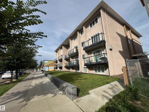 Multi-level building with stucco exterior, private balconies featuring glass railings, and a manicured lawn - #209 11429 124 St Nw, Edmonton, AB 