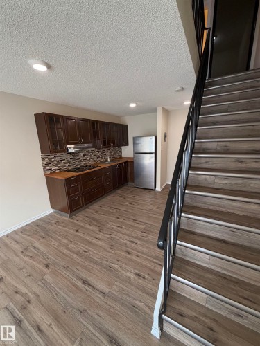 Wood-finish flooring throughout, full kitchen with dark wood-finish cabinetry, stainless steel appliances, and a mosaic tile backsplash - #209 11429 124 St Nw, Edmonton, AB 