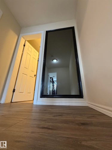 Wood-finish flooring with white baseboards, featuring a full-length wall mirror with a black frame - #209 11429 124 St Nw, Edmonton, AB 