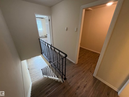 Staircase with wrought iron railing, wood-finish flooring, and neutral wall tones - #209 11429 124 St Nw, Edmonton, AB 