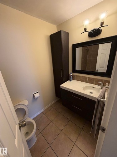 Tile flooring, wall-mounted vanity with integrated sink, framed mirror, vertical storage cabinet, and a two-light fixture - #209 11429 124 St Nw, Edmonton, AB 