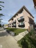 Multi-story building featuring stucco exterior, multiple balconies with glass railings, and a sloped lawn with a retaining wall - #209 11429 124 St Nw, Edmonton, AB 