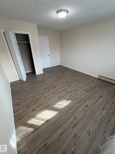 Wood-finish flooring, neutral wall paint, ceiling-mounted light fixture, and a built-in closet with bi-fold doors - #209 11429 124 St Nw, Edmonton, AB 