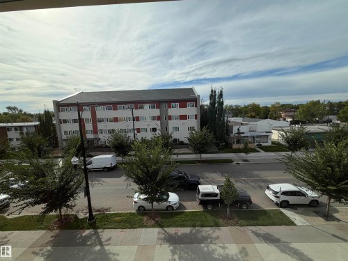 Urban streetscape featuring mature trees and a multi-story building with a red and white facade - #209 11429 124 St Nw, Edmonton, AB 