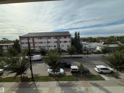 Urban streetscape featuring mature trees and a multi-story building with a red and white facade - 