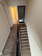 Wood-finish flooring throughout the hallway and stair treads, featuring a contrasting black metal handrail and white trim - 