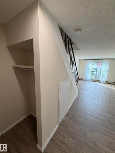 Built-in open shelving with hanging rod, wood-finish flooring, white baseboards, and a black wrought iron stair railing - #209 11429 124 St Nw, Edmonton, AB 