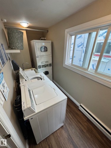 Laundry area featuring wood-finish flooring, a white-framed window, a built-in wall shelf, and an overhead light fixture - #209 11429 124 St Nw, Edmonton, AB 