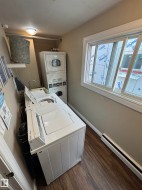 Laundry area featuring wood-finish flooring, a white-framed window, a built-in wall shelf, and an overhead light fixture - 