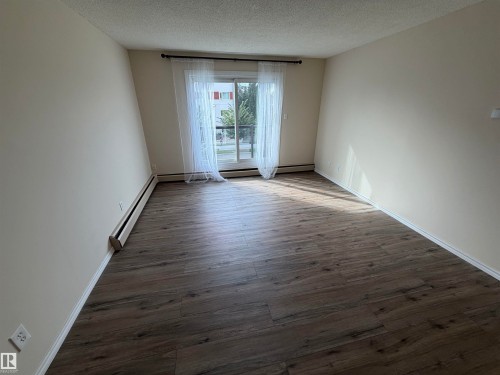 Wood-finish flooring throughout, neutral wall color, and a sliding glass door with a transom window - #209 11429 124 St Nw, Edmonton, AB 