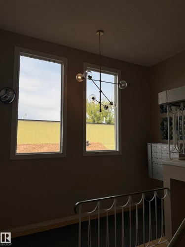 Two vertical windows with white trim, modern multi-bulb chandelier, and metal staircase railing - #209 11429 124 St Nw, Edmonton, AB 