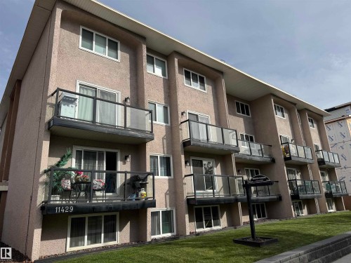 Multi-level building with stucco exterior, multiple units featuring individual balconies with glass railings, and expansive windows - #209 11429 124 St Nw, Edmonton, AB 