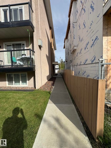 Exterior building with stucco finish, private balcony with glass railing, ground-level lawn area, concrete walkway, and wood fencing - #209 11429 124 St Nw, Edmonton, AB 