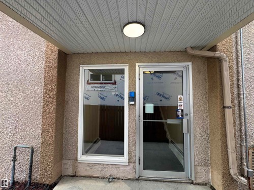 Stucco exterior with a covered entry, featuring a recessed light fixture and a full-light entry door - #209 11429 124 St Nw, Edmonton, AB 