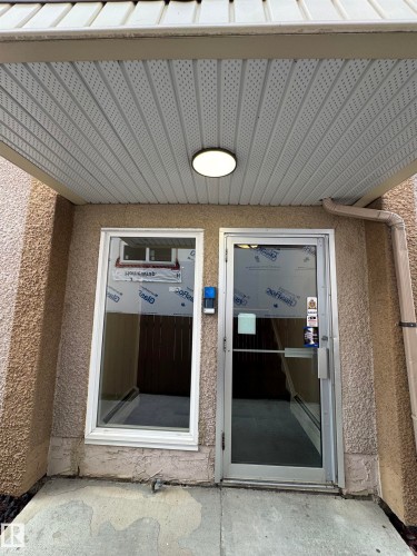 Entry featuring a stucco exterior, a protected overhead soffit with recessed lighting, an aluminum-framed glass door, and an adjacent window - #209 11429 124 St Nw, Edmonton, AB 