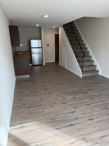 Wood-finish flooring, recessed ceiling lighting, open-tread staircase with wrought iron railing, stainless steel refrigerator, and dark wood-finish cabinetry - #209 11429 124 St Nw, Edmonton, AB 