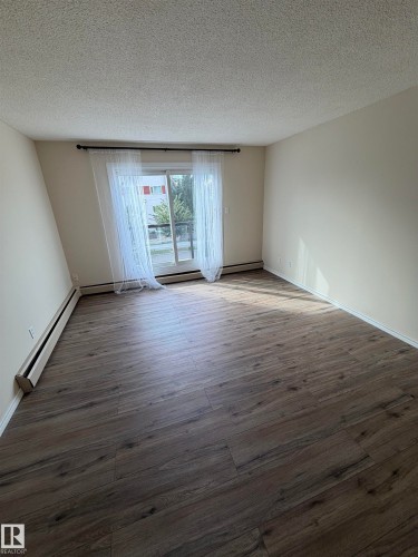 Spacious room with wood-finish flooring and neutral wall tones - #209 11429 124 St Nw, Edmonton, AB 