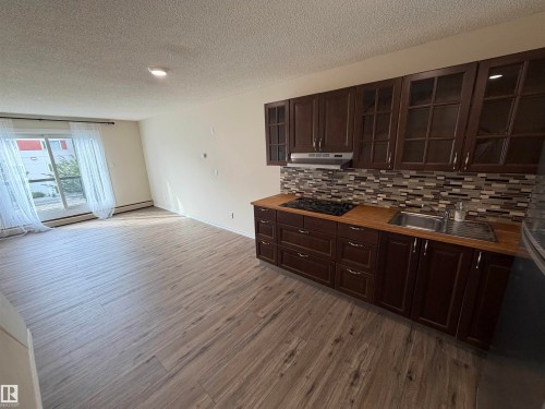 Wood-finish flooring throughout, full kitchen with wood cabinetry and a tiled backsplash, and sliding glass doors - #209 11429 124 St Nw, Edmonton, AB 