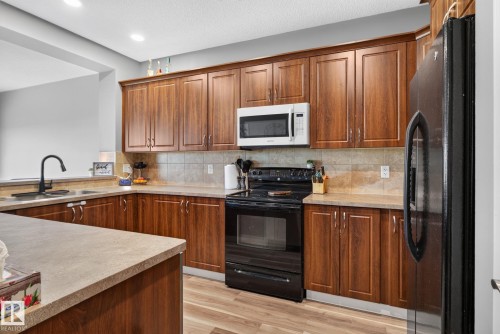 Kitchen featuring wood-finish cabinetry, a black range, white microwave, black refrigerator, and a stainless steel sink with a matte black faucet - 385 Simmonds Way, Leduc, AB - Indoor Photo Showing Kitchen