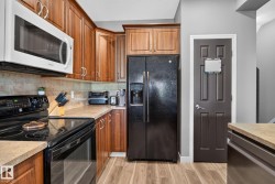 Kitchen featuring wood-finish cabinetry, light-toned countertops, and black appliances - 
