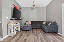 Spacious living area featuring light gray walls, wood-finish flooring, a ceiling fan with integrated lighting, and white baseboards - 