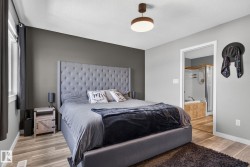 Spacious bedroom with wood-finish flooring, a contemporary ceiling light fixture, and an open doorway revealing a bathroom with a built-in tub and shower enclosure - 