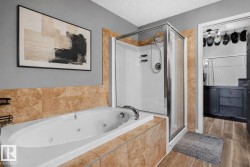 Bathroom featuring a built-in jetted tub with tile surround, a glass-enclosed shower, and wood-finish flooring - 