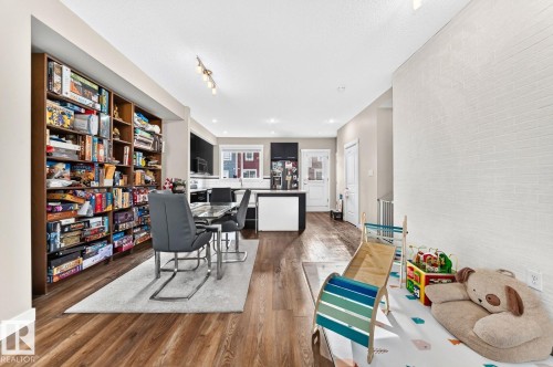 Wood-finish flooring, built-in shelving, kitchen with dark cabinetry, white subway tile wall, and track lighting - #20 8315 180 Av Nw, Edmonton, AB 
