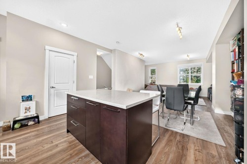 Open-concept living area with wood-finish flooring, recessed lighting, a kitchen island with stone countertop, and built-in shelving - #20 8315 180 Av Nw, Edmonton, AB 