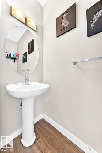 Pedestal sink with chrome faucet, wood-finish flooring, and a circular mirror - #20 8315 180 Av Nw, Edmonton, AB 