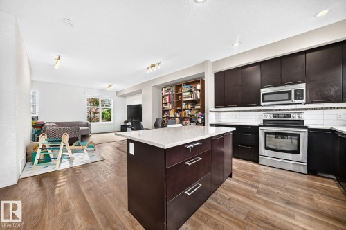 Kitchen island with a light-colored countertop, stainless steel appliances, dark wood-finish cabinetry, and wood-finish flooring - #20 8315 180 Av Nw, Edmonton, AB 