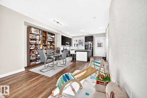 Open-concept floor plan featuring wood-finish flooring, a built-in shelving unit, recessed lighting, and a kitchen with dark cabinetry - #20 8315 180 Av Nw, Edmonton, AB 