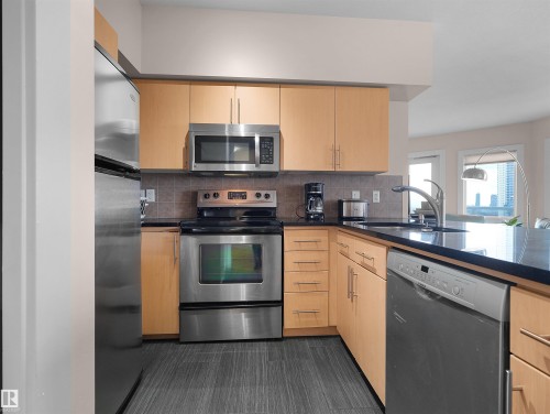 Kitchen featuring stainless steel appliances, wood-finish cabinetry, dark countertops, and a tiled backsplash - #1601 10136 104 St Nw, Edmonton, AB 