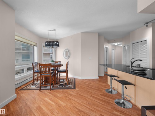 Spacious open-concept living area with wood-finish flooring, a kitchen island with seating, and a dining area with a chandelier - #1601 10136 104 St Nw, Edmonton, AB 