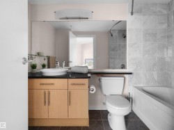 Wood-finish vanity with a vessel sink, black countertop, full-height mirror, white bathtub, and large format tiled shower surround - 