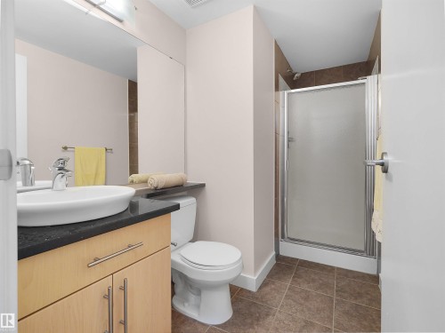 Modern vanity with a vessel sink, dark countertop, light wood-finish cabinetry, and a shower stall with a framed frosted glass door - #1601 10136 104 St Nw, Edmonton, AB 