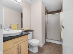 Modern vanity with a vessel sink, dark countertop, light wood-finish cabinetry, and a shower stall with a framed frosted glass door - 