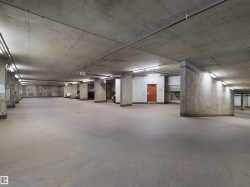 Concrete parking area with exposed concrete ceilings and columns, featuring fluorescent strip lighting and an orange door - 