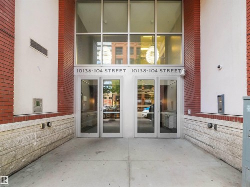 Building facade featuring red brick and light-toned panels, a stone-finish base, dual glass entry doors, and a multi-pane transom window - #1601 10136 104 St Nw, Edmonton, AB 