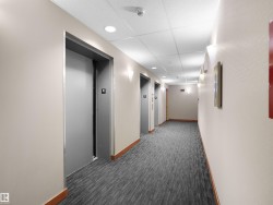 Corridor featuring multiple elevators with metallic doors, recessed ceiling lighting, wall-mounted sconces, and wood-finish baseboards - 
