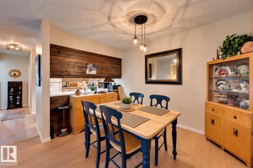 Light wood-finish flooring, accent wall with horizontal wood paneling, contemporary pendant lighting fixture, and a built-in wall mirror - #203 24 Alpine Pl, St. Albert, AB 