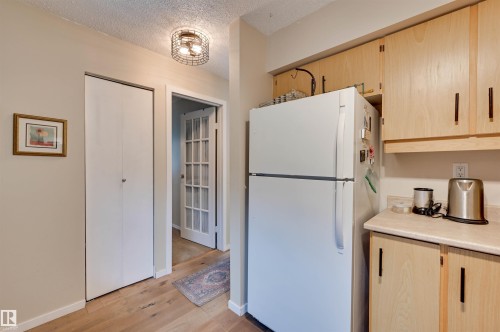 Light wood-finish flooring, bi-fold closet doors, French-pane glass door, natural wood cabinetry, and a wire cage flush mount ceiling light - #203 24 Alpine Pl, St. Albert, AB 