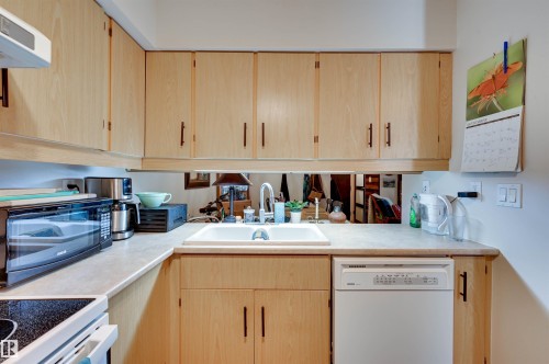 Wood-finish cabinetry with dark hardware, a white sink, and light-toned countertops - #203 24 Alpine Pl, St. Albert, AB 