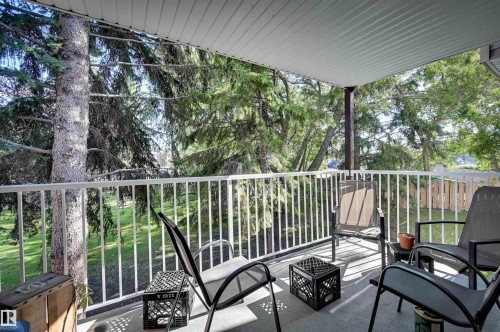 Covered balcony with a concrete surface and white metal railings, surrounded by mature trees - #203 24 Alpine Pl, St. Albert, AB 